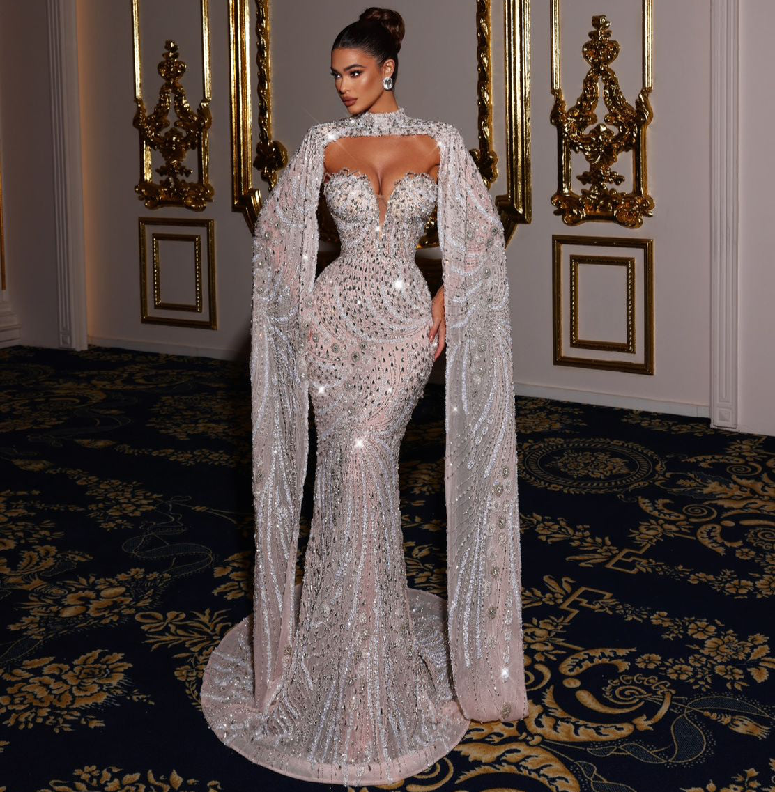 Woman in a sparkling evening gown standing in an opulent room with decorative mirrors.