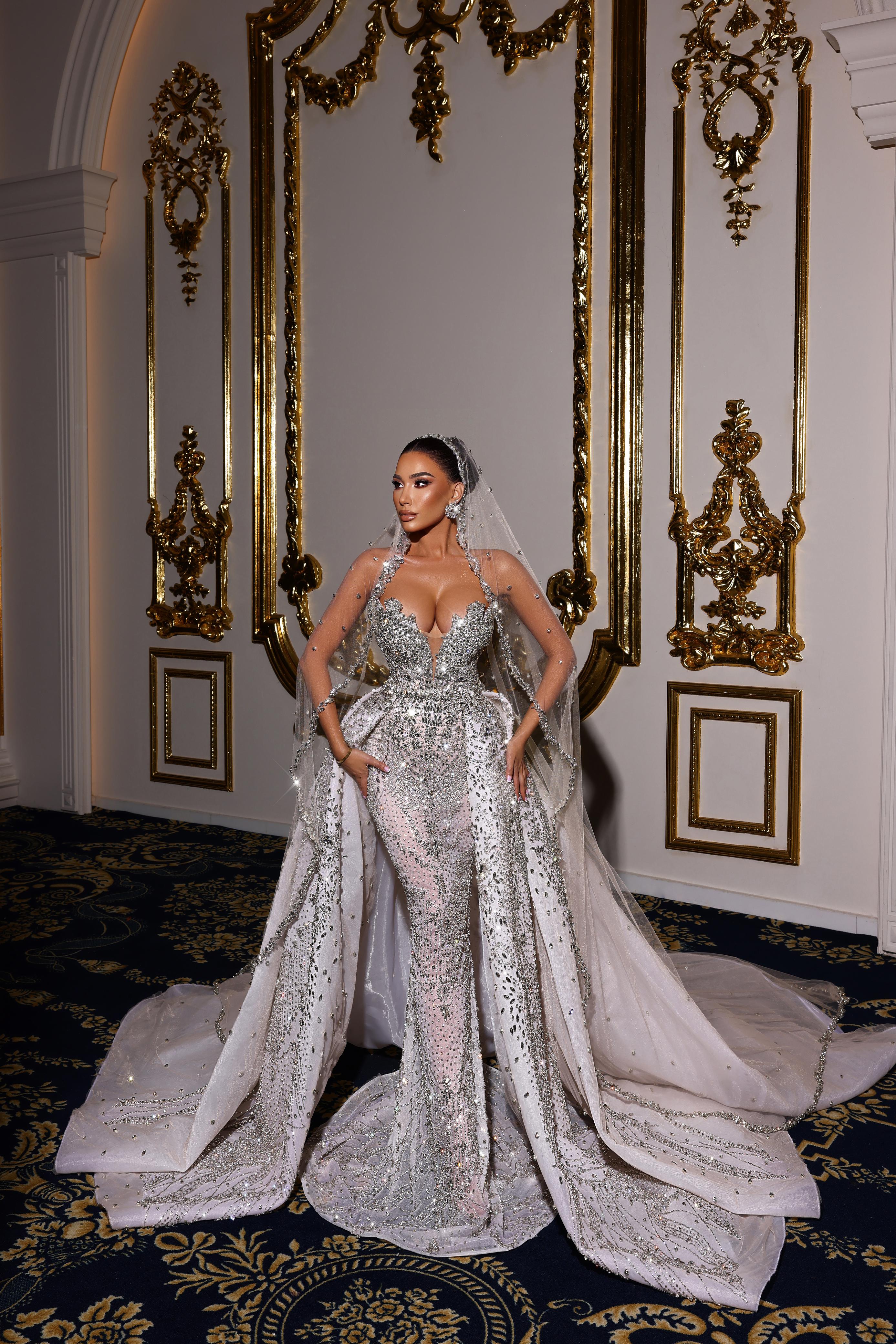 Woman in a sparkling silver wedding gown standing in an opulent room with decorative mirrors.