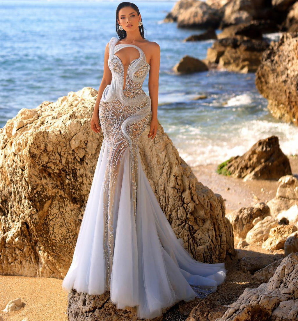 Woman in a white wedding dress standing on rocks by the ocean