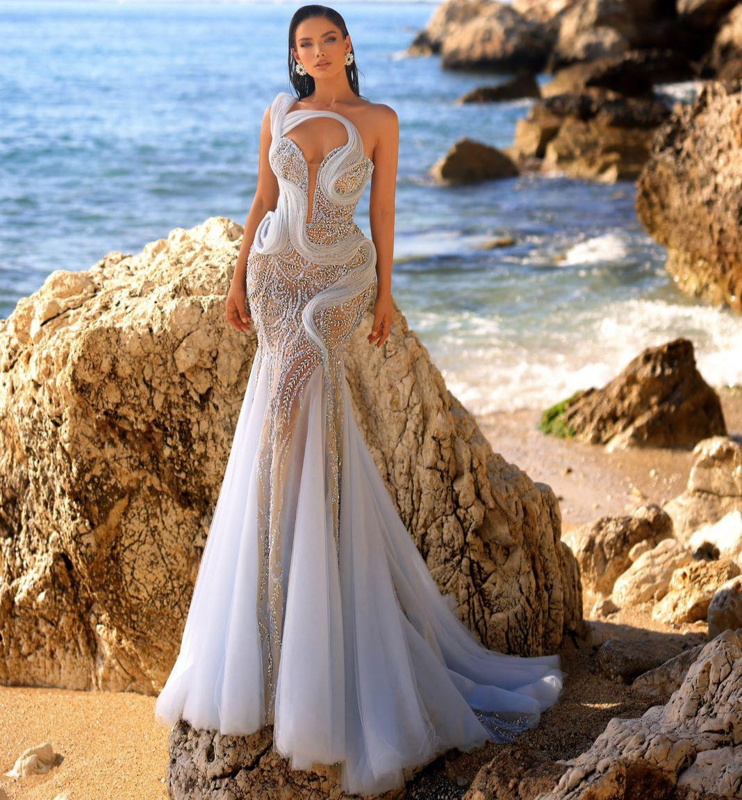 Woman in a white wedding dress standing on rocks by the ocean