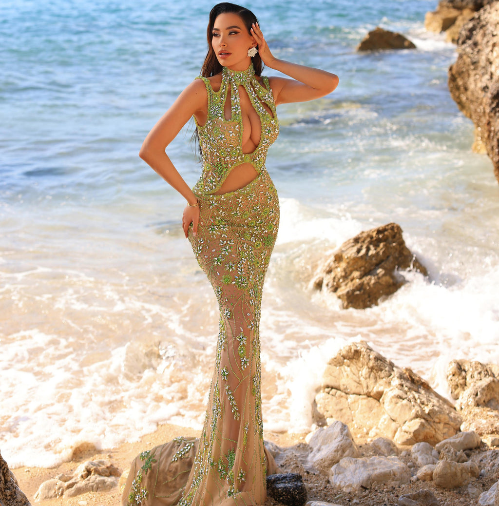 Woman in a green evening gown standing on a rocky beach with ocean in the background