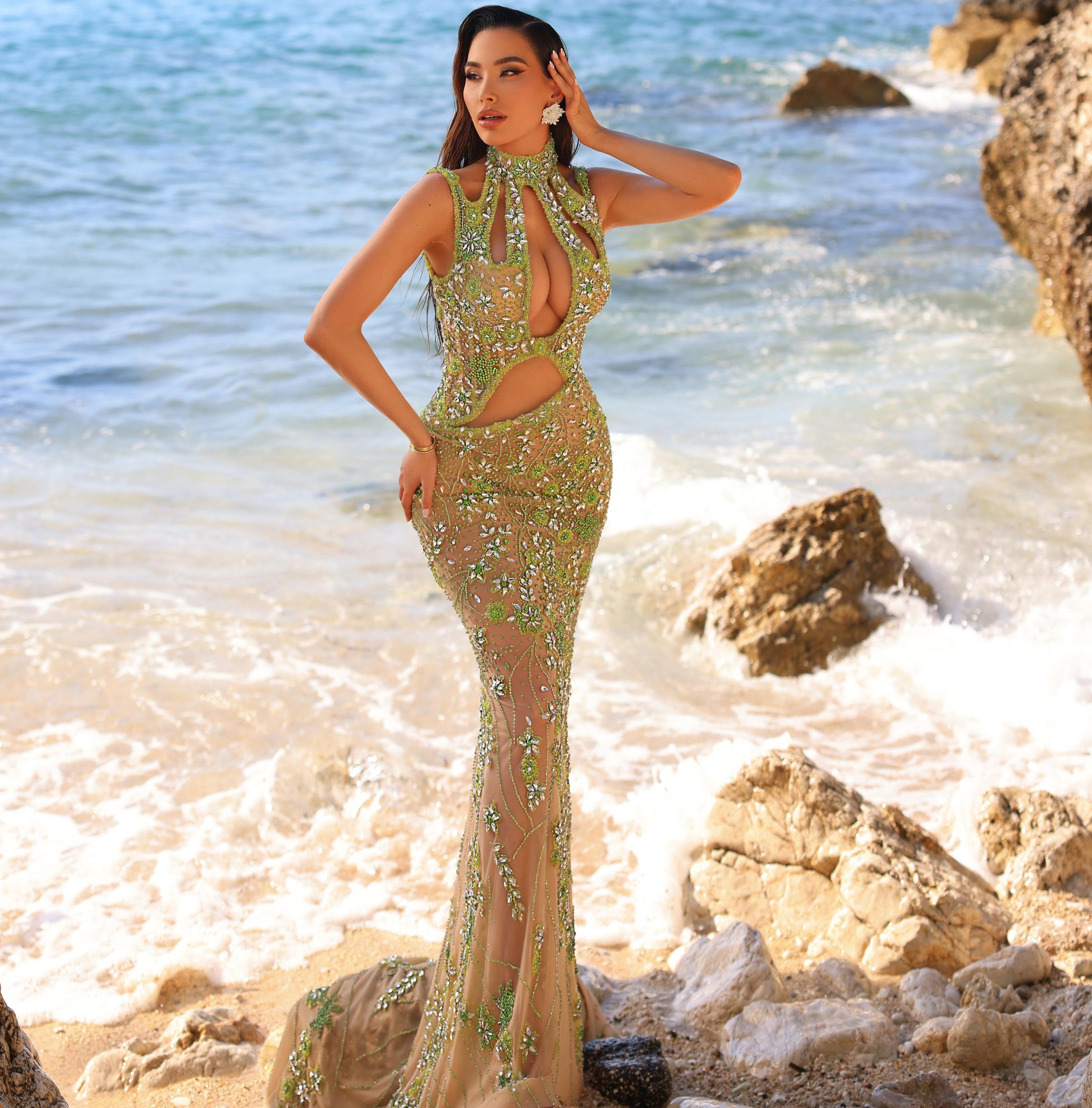 Woman in a green evening gown standing on a rocky beach with ocean in the background