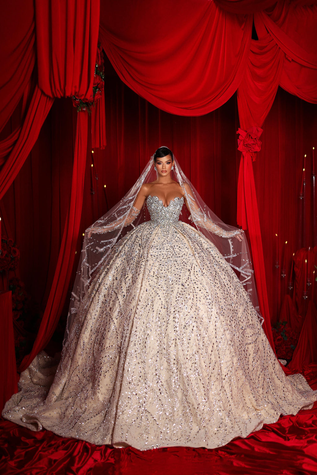 Woman in a sparkling wedding gown with a long veil against red curtains