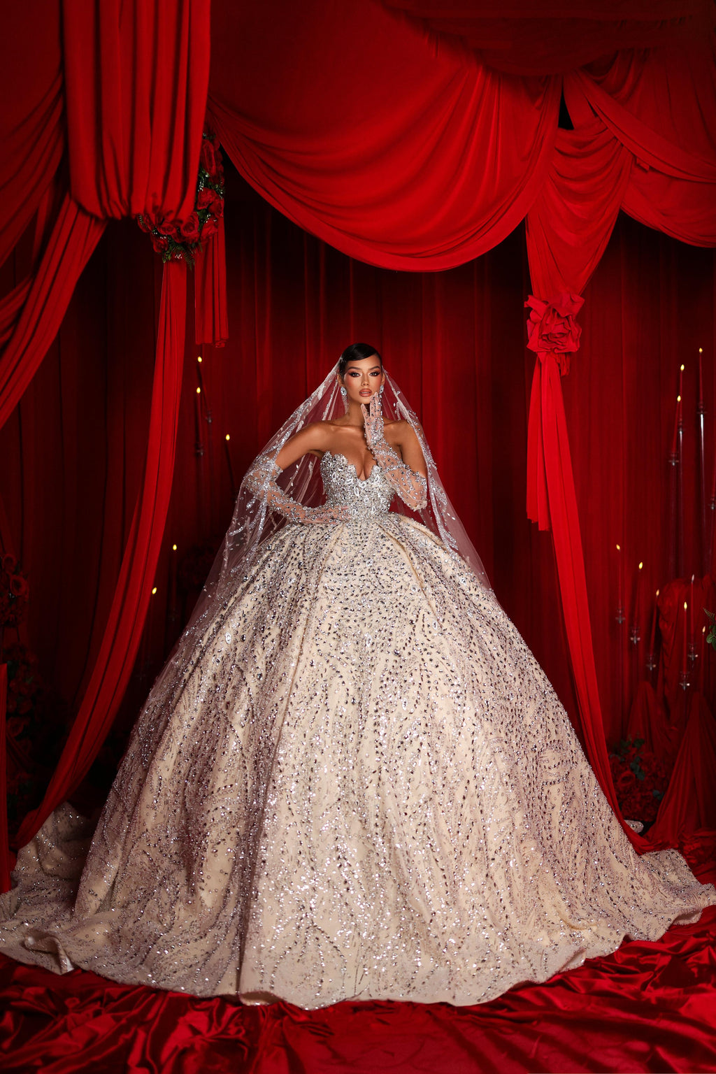 Woman in a sparkling wedding gown with a veil against red curtains