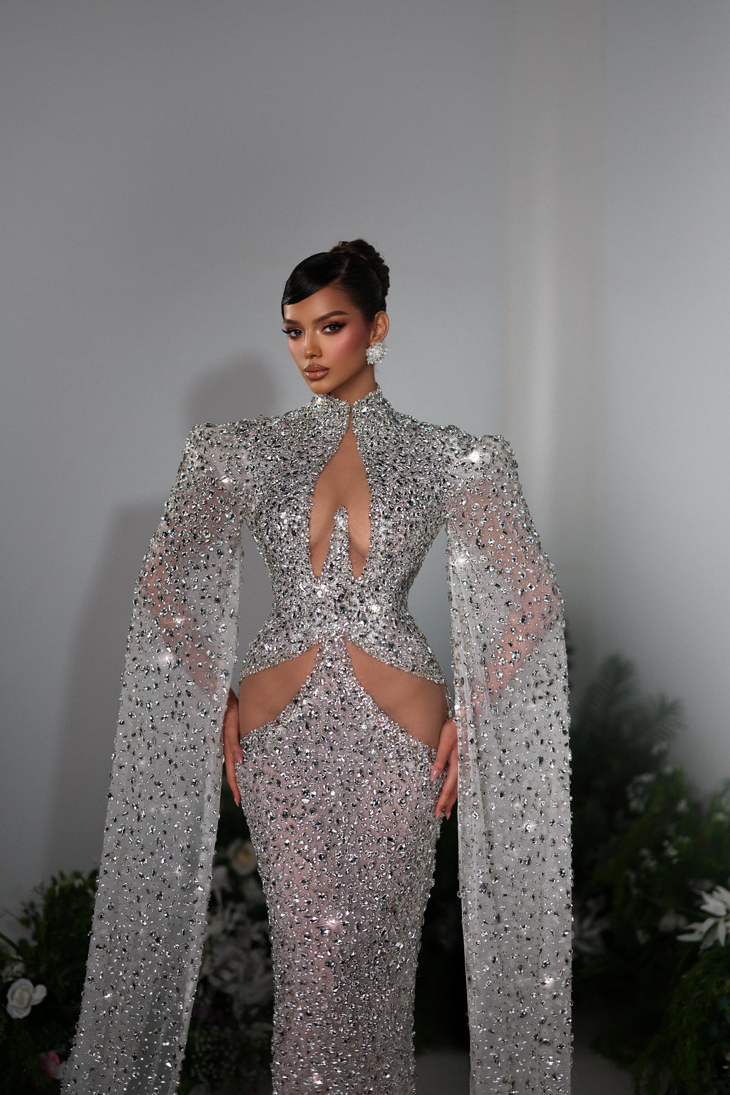 Person wearing a sparkling silver gown with a long train in a decorated indoor setting.