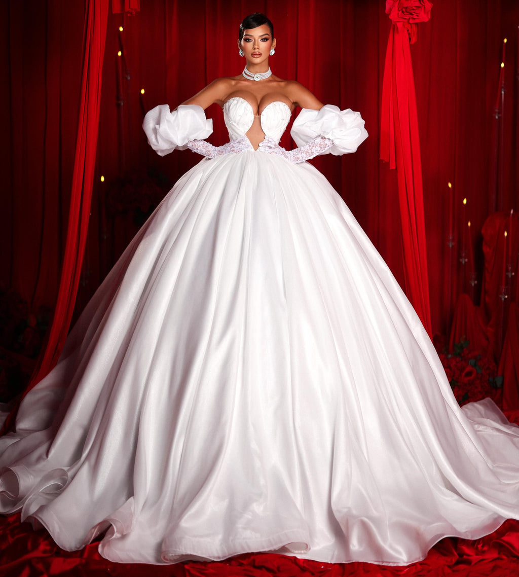 Woman in a white gown standing in front of red curtains