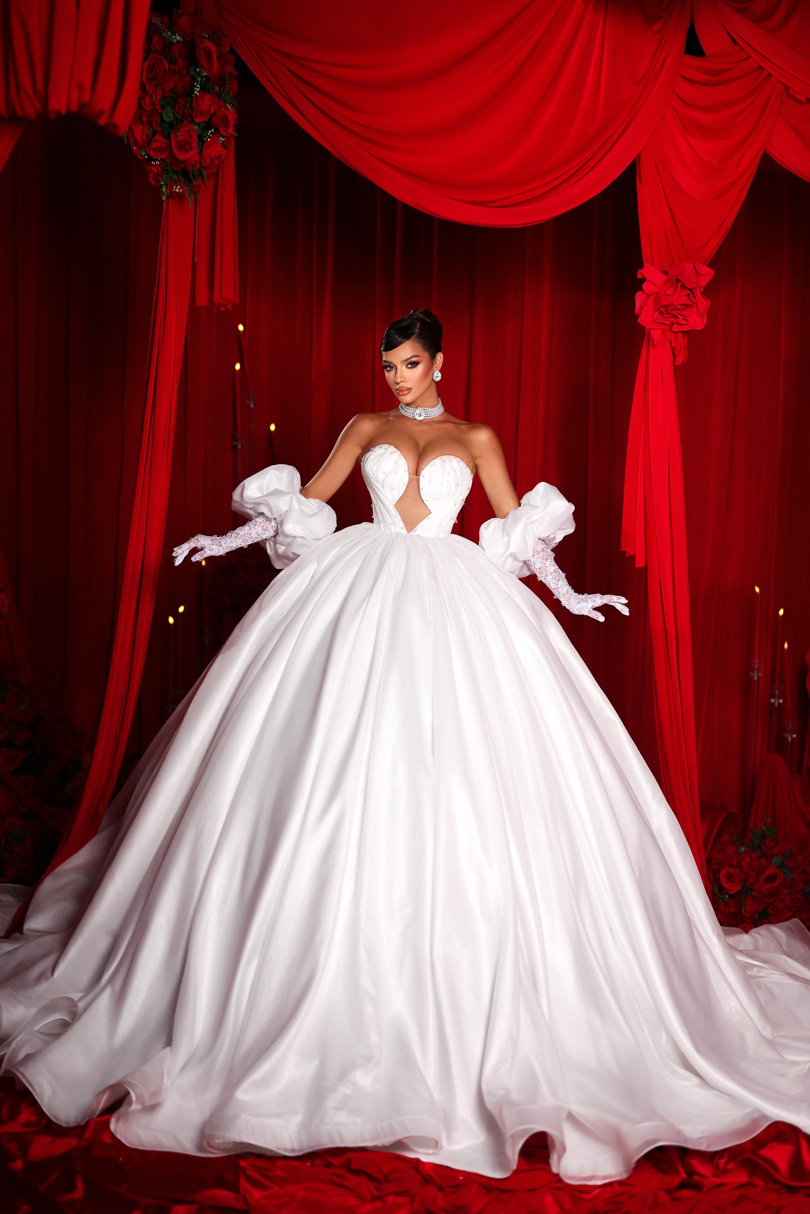 White wedding dress with large bow details against a red curtain backdrop