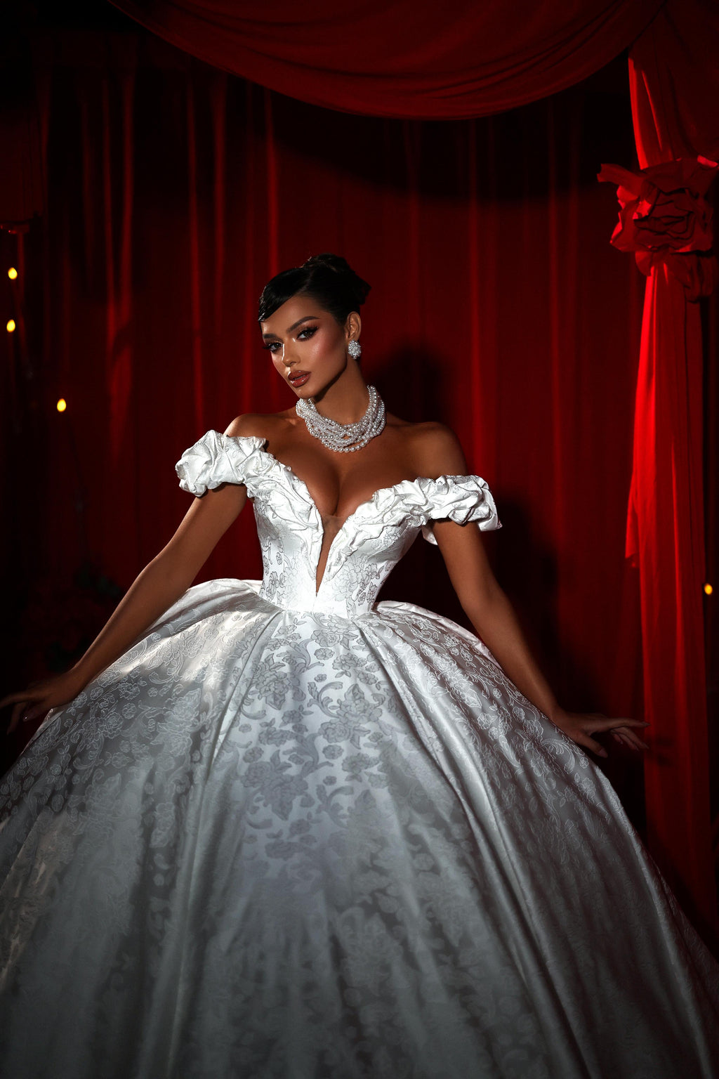 Woman in a white wedding gown with a deep neckline against a red curtain backdrop