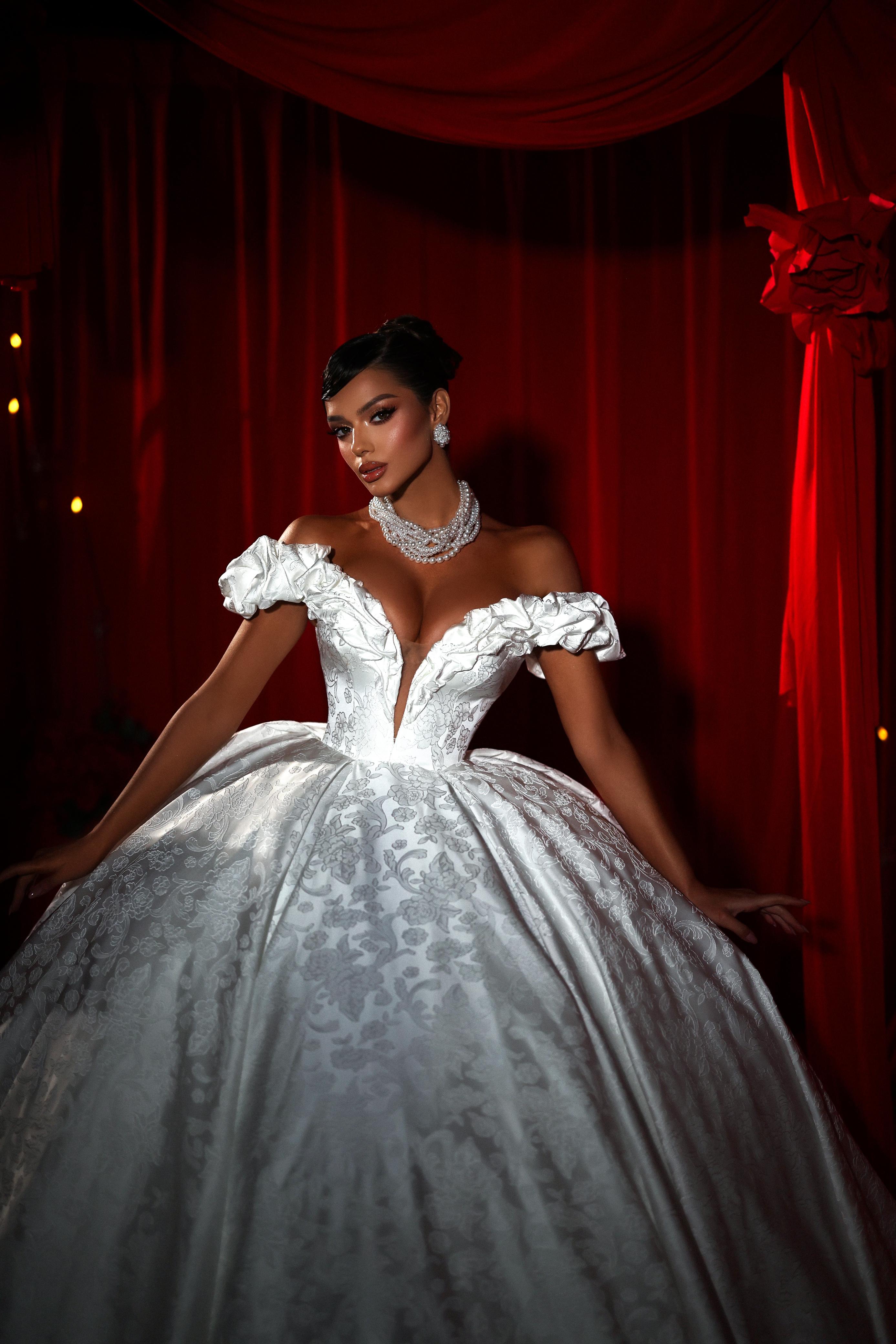 Woman in a white wedding gown with a deep neckline against a red curtain backdrop