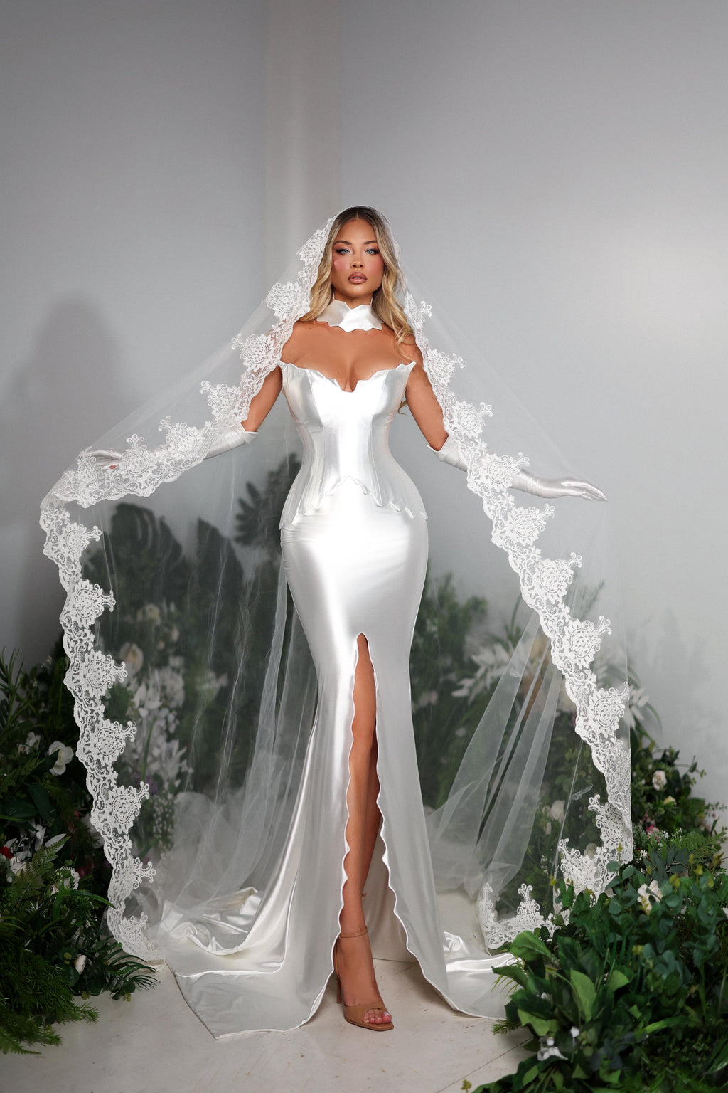 Woman in a white wedding dress with a long veil standing against a gray background.