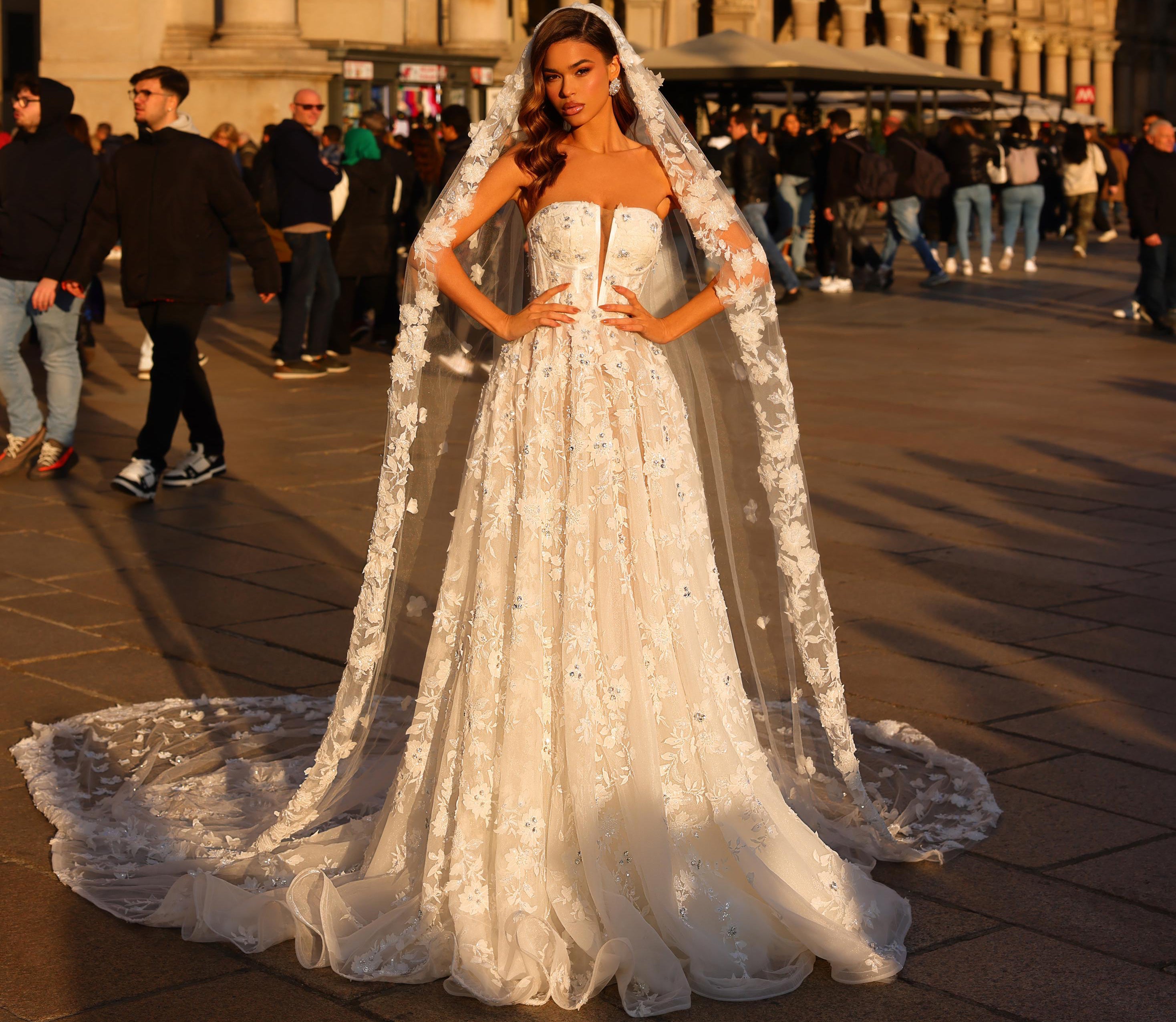Woman in a white wedding dress with a long train standing in an urban setting.