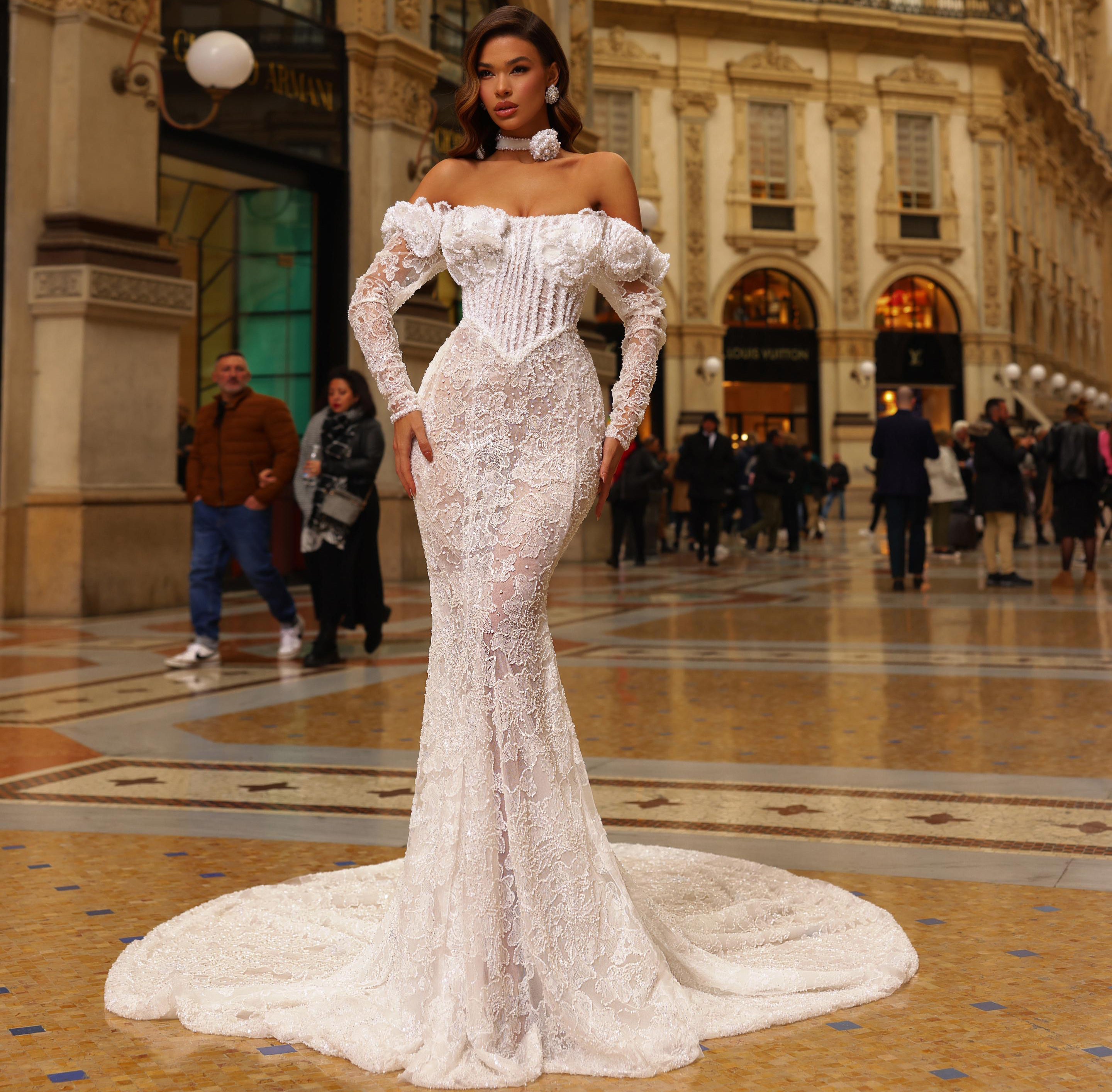 Woman in a white lace dress standing in an ornate indoor setting with people around