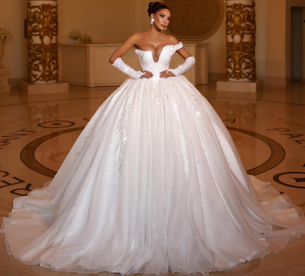 Woman in a white wedding dress standing in an elegant indoor setting with chandelier.