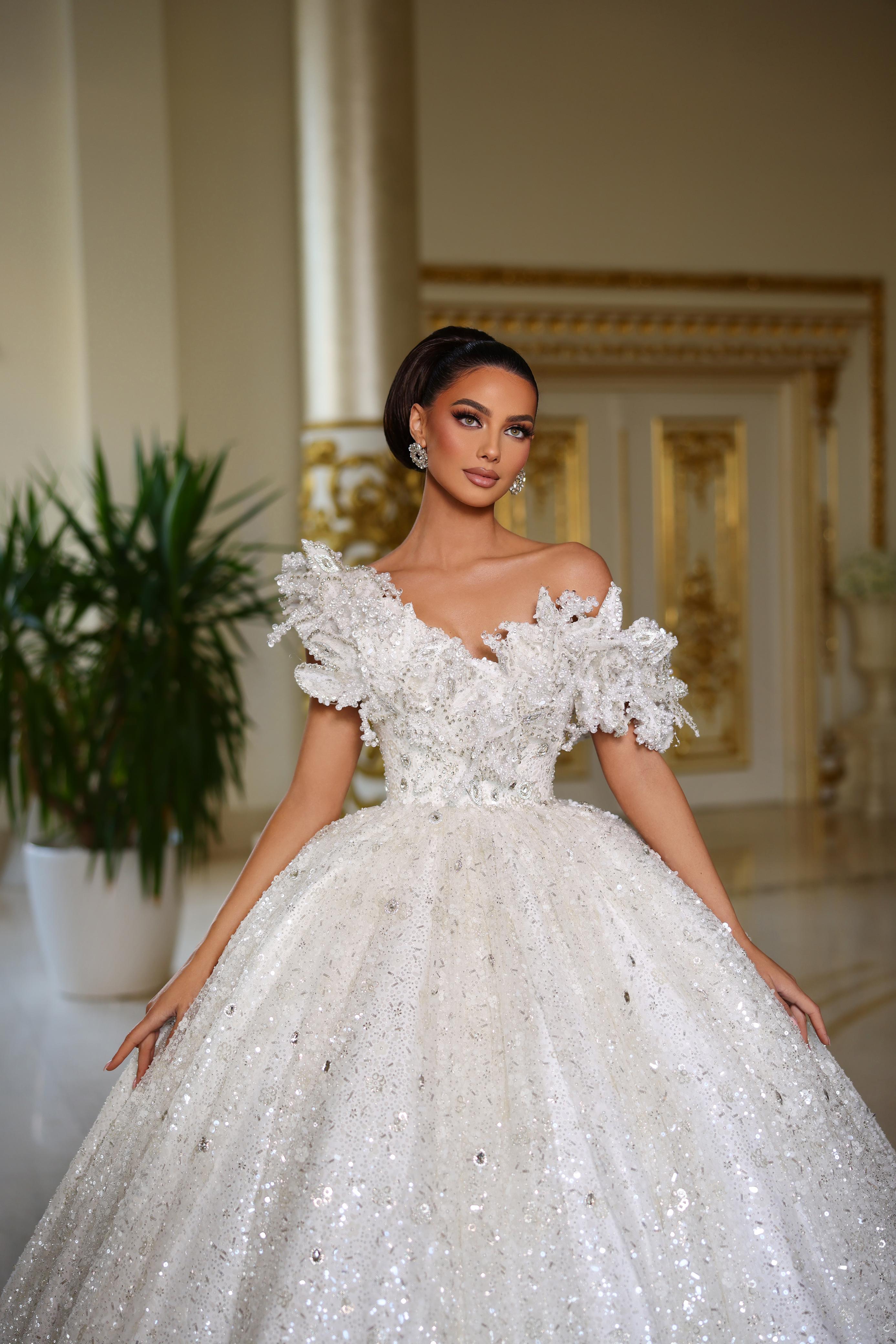 Woman in a white wedding dress standing in an elegant interior setting.