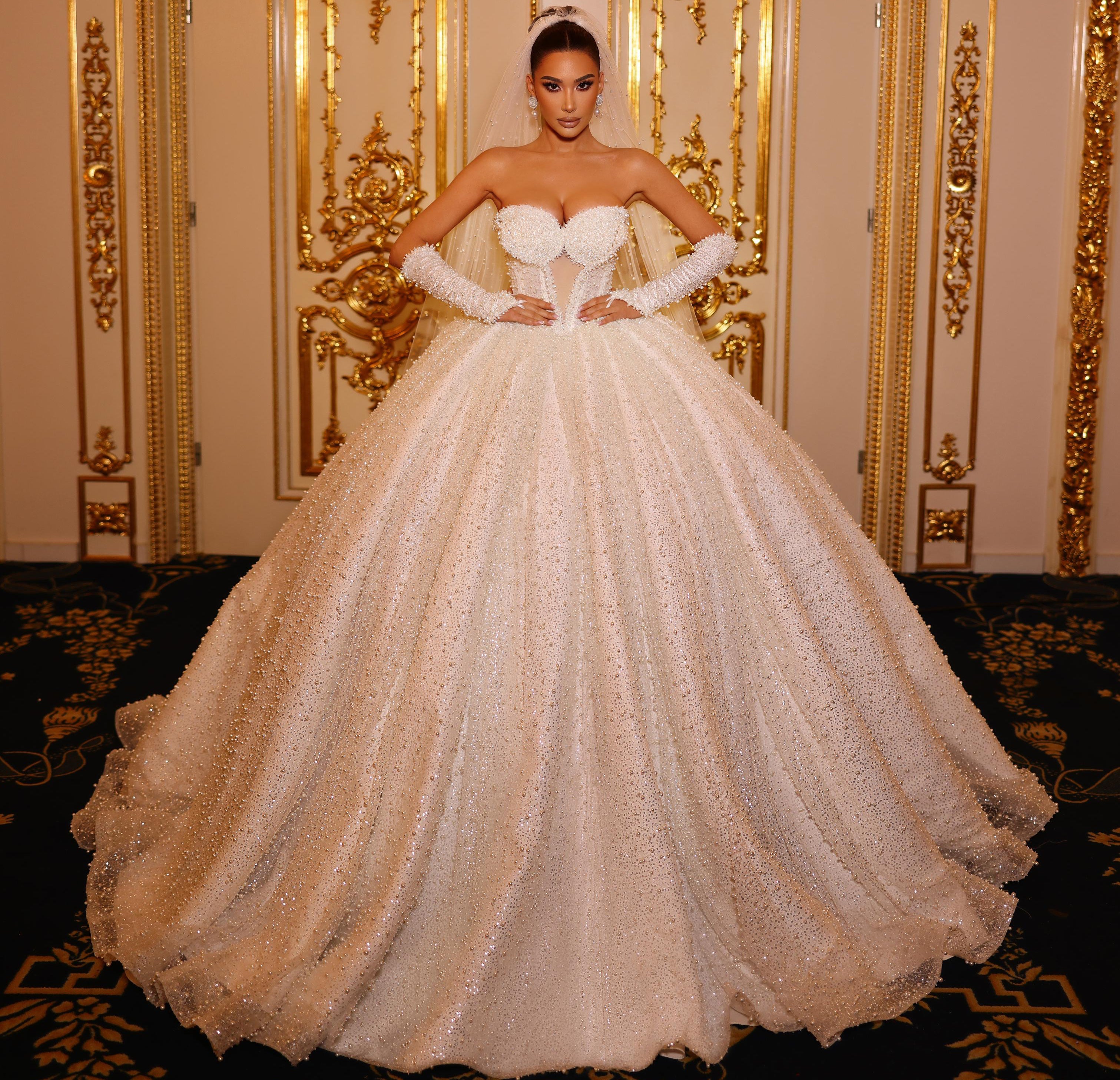 Woman in a white strapless gown with a full skirt standing in an ornate room.