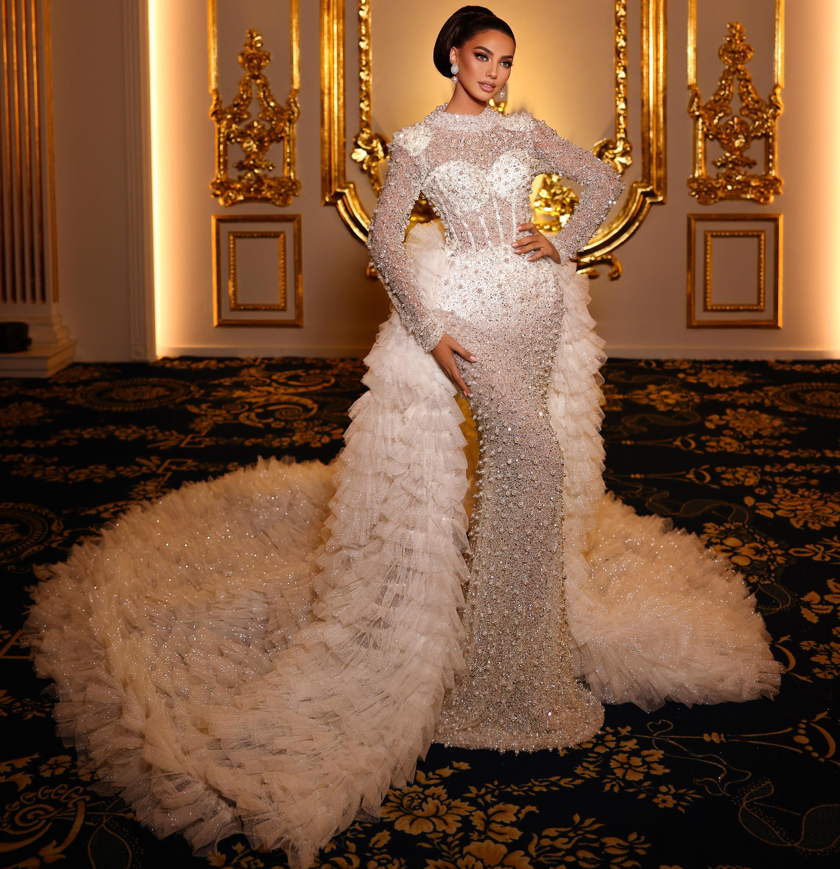 Woman in a white evening gown with feathered skirt standing in an ornate room.