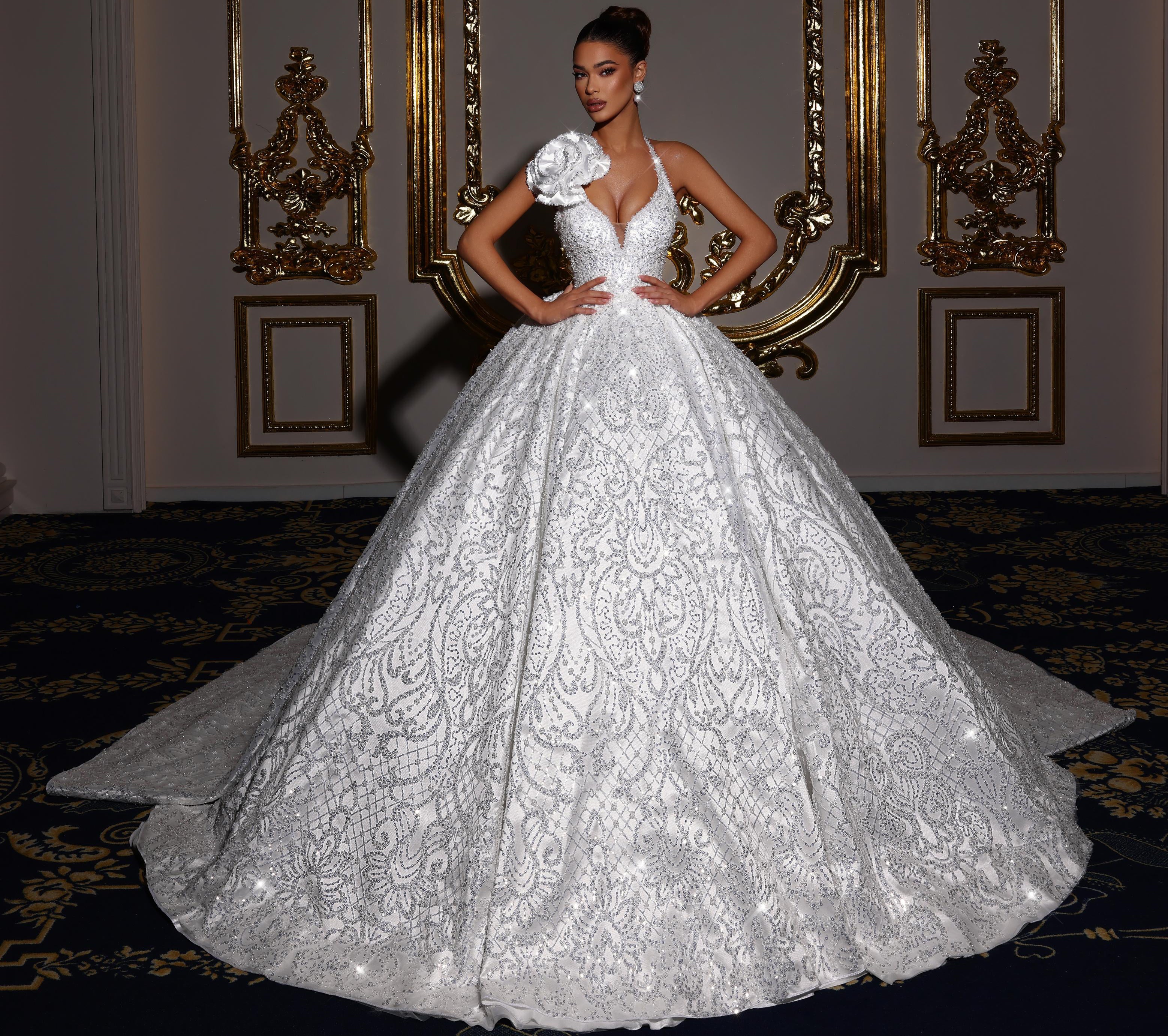 Woman in a white lace wedding dress standing in an ornate room with decorative mirrors.
