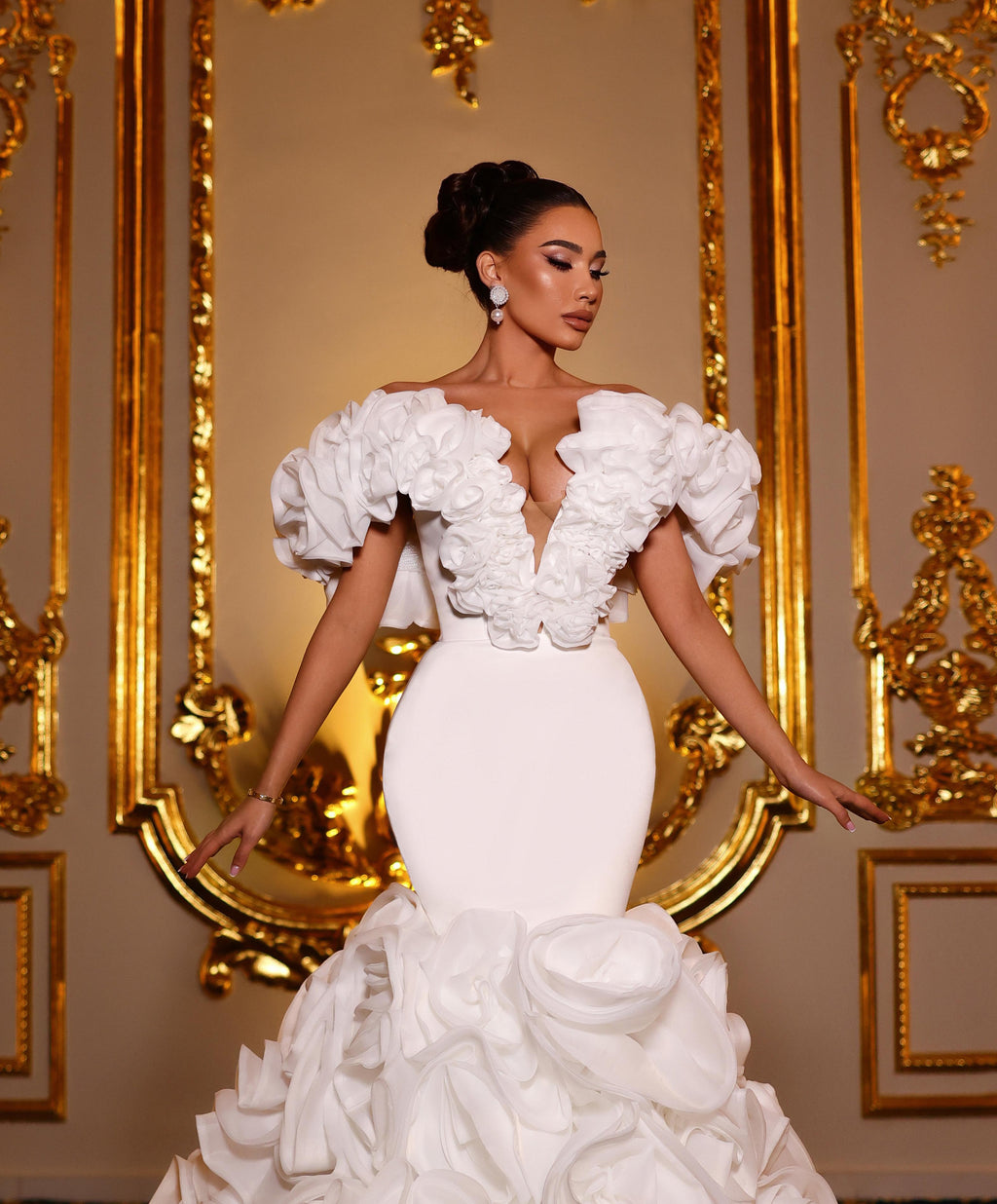 Woman in a white wedding dress standing in front of ornate gold mirrors.