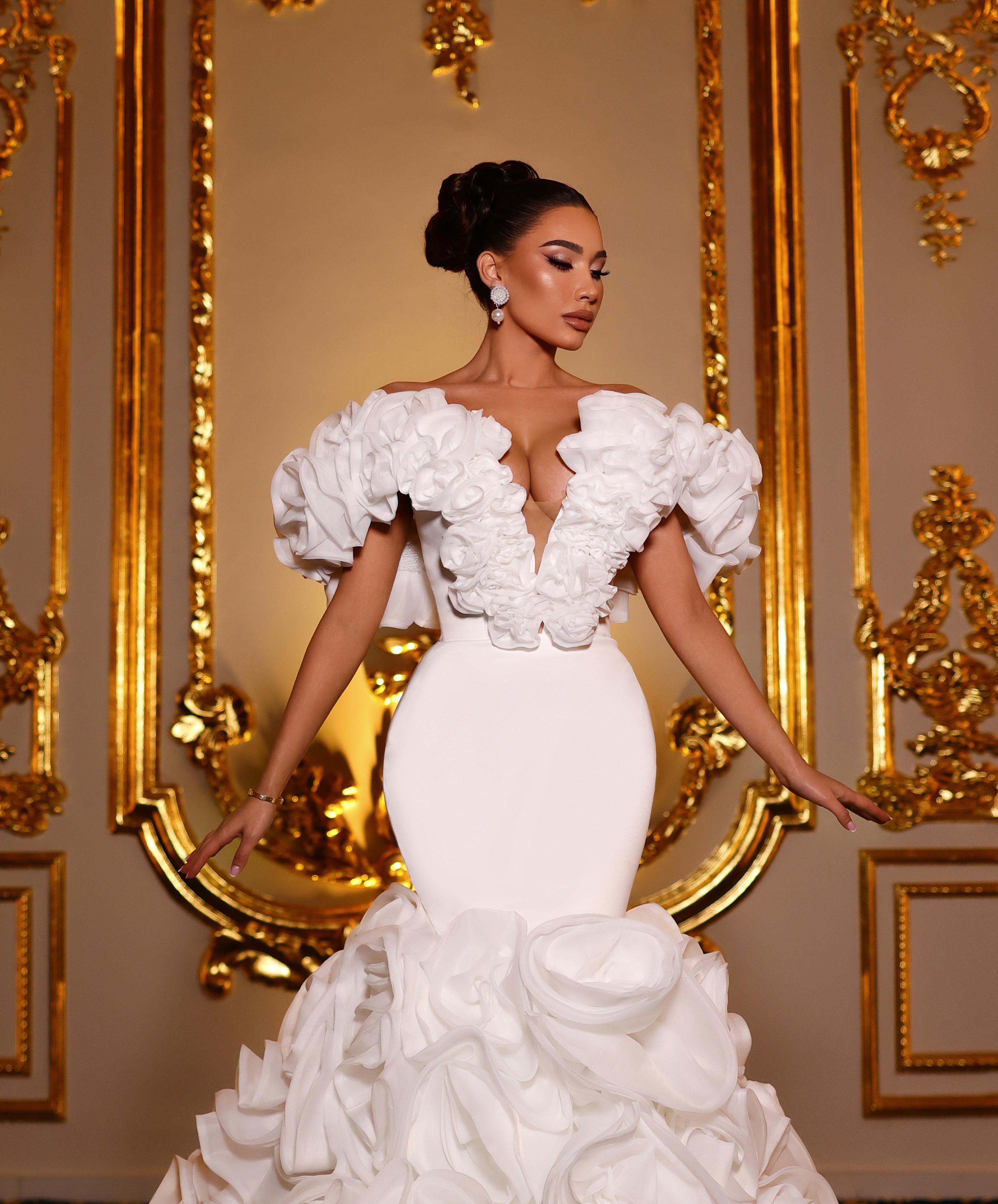 Woman in a white wedding dress standing in front of ornate gold mirrors.