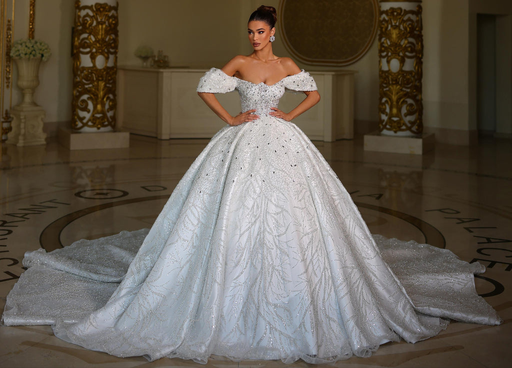 Woman in a white wedding dress standing in an elegant room with a chandelier.