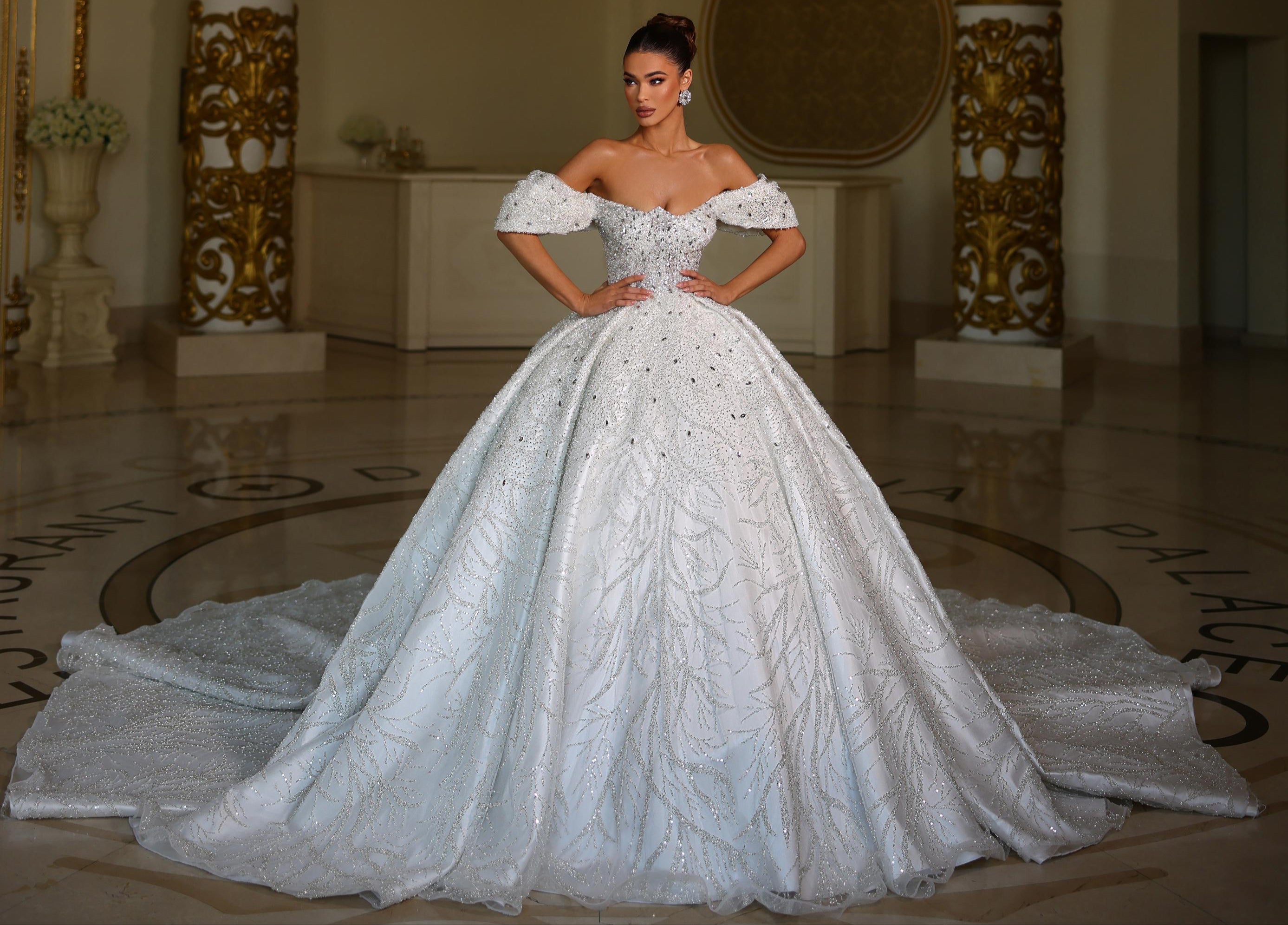 Woman in a white wedding dress standing in an elegant room with a chandelier.