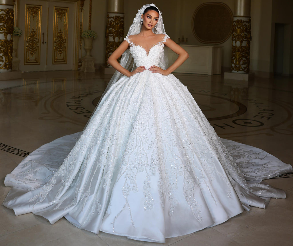 Woman in a white wedding dress standing in an elegant indoor setting with a chandelier.
