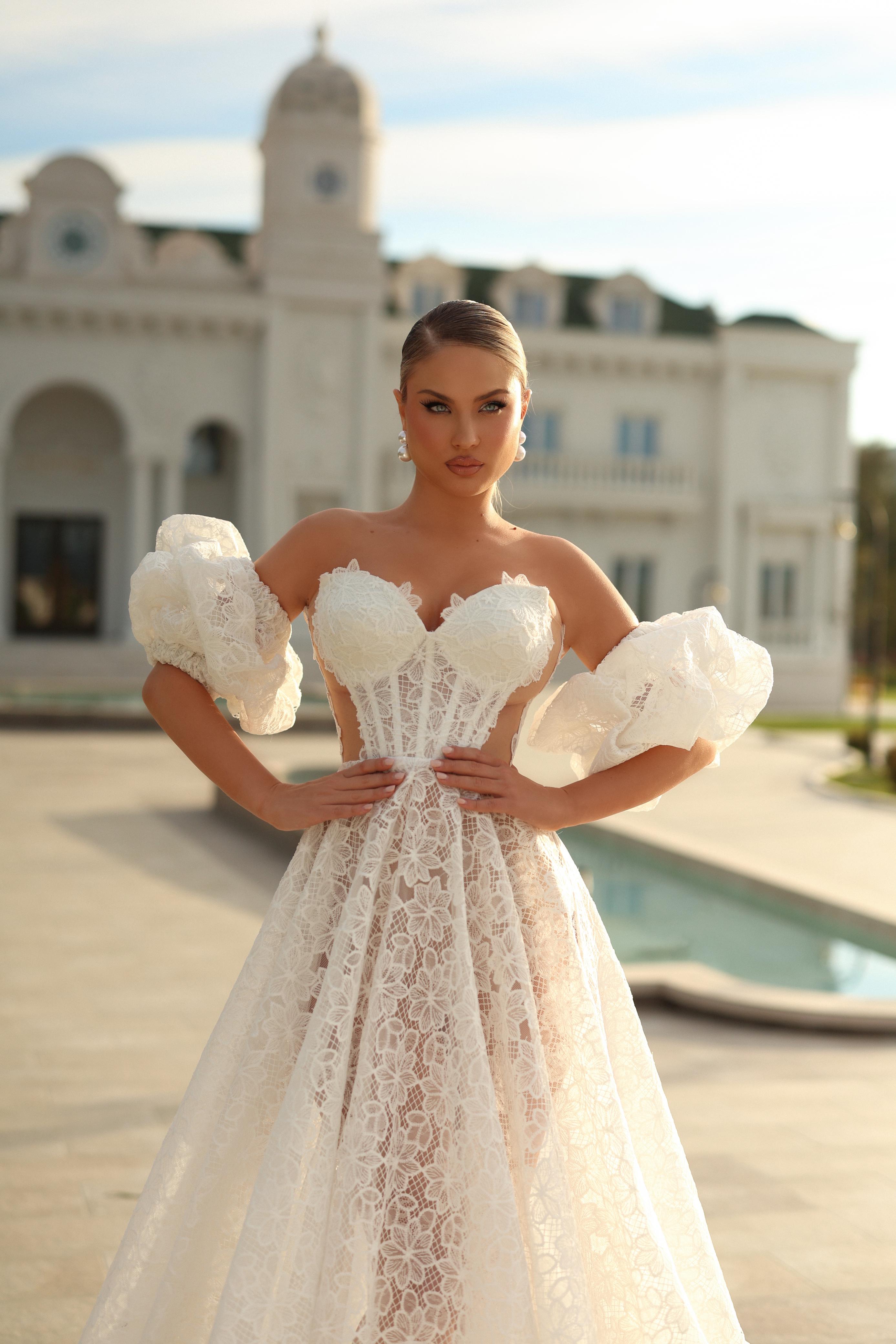 Woman in a white lace wedding dress holding flowers in front of a classical building.