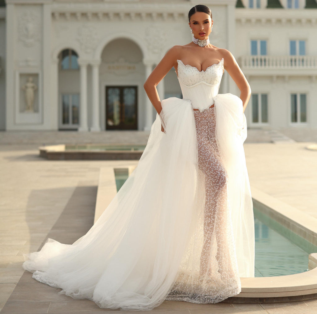 Woman in a white wedding dress standing in front of a classical building with a pool.