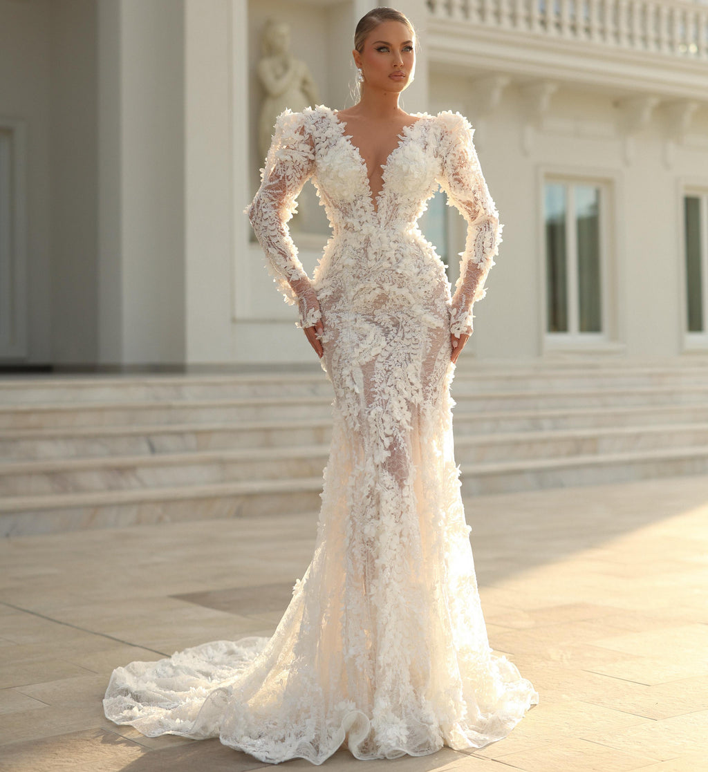Woman in a white lace wedding dress standing in front of an elegant building.