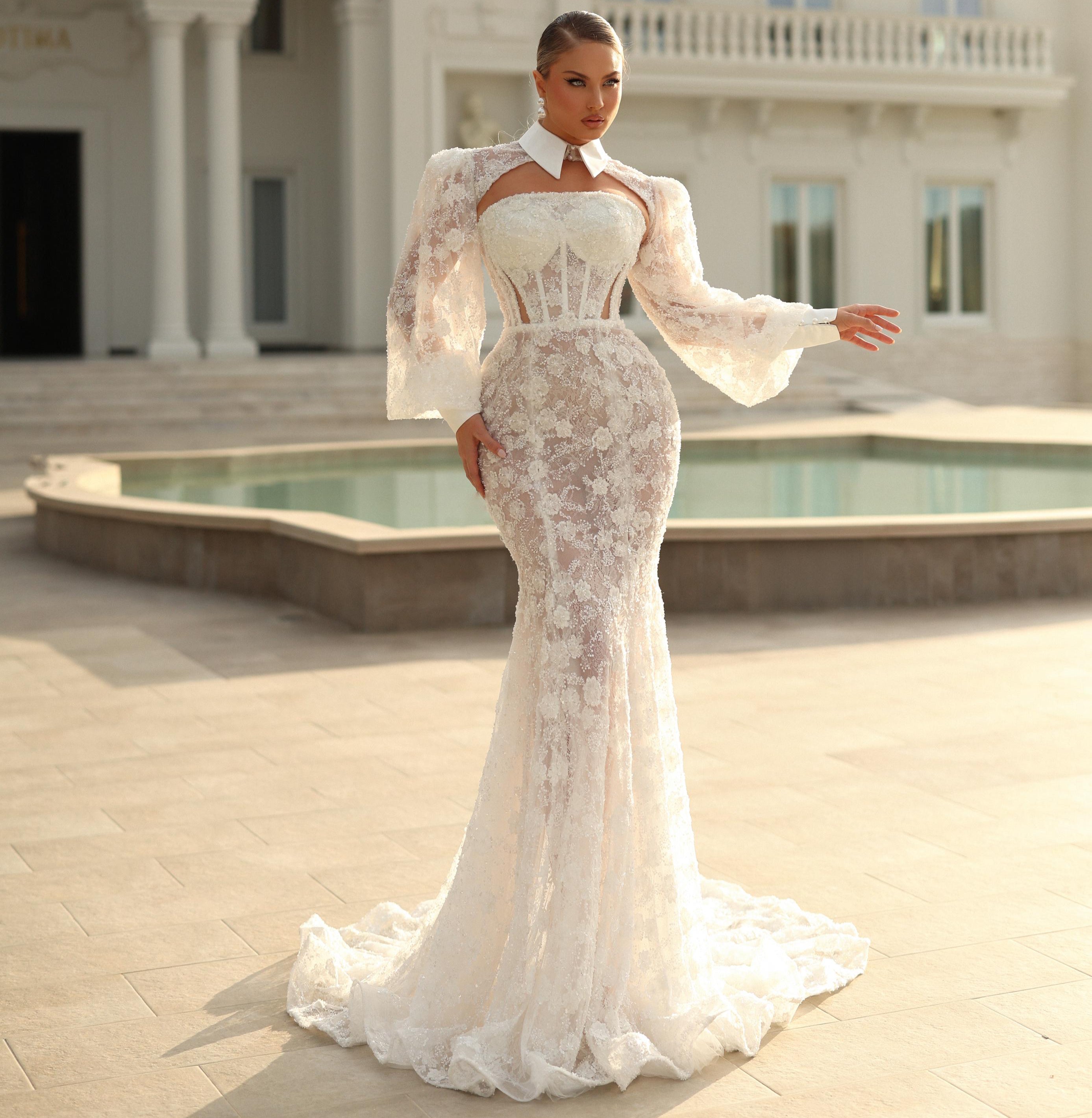 Woman in a white lace dress standing in front of an elegant building with a pool.