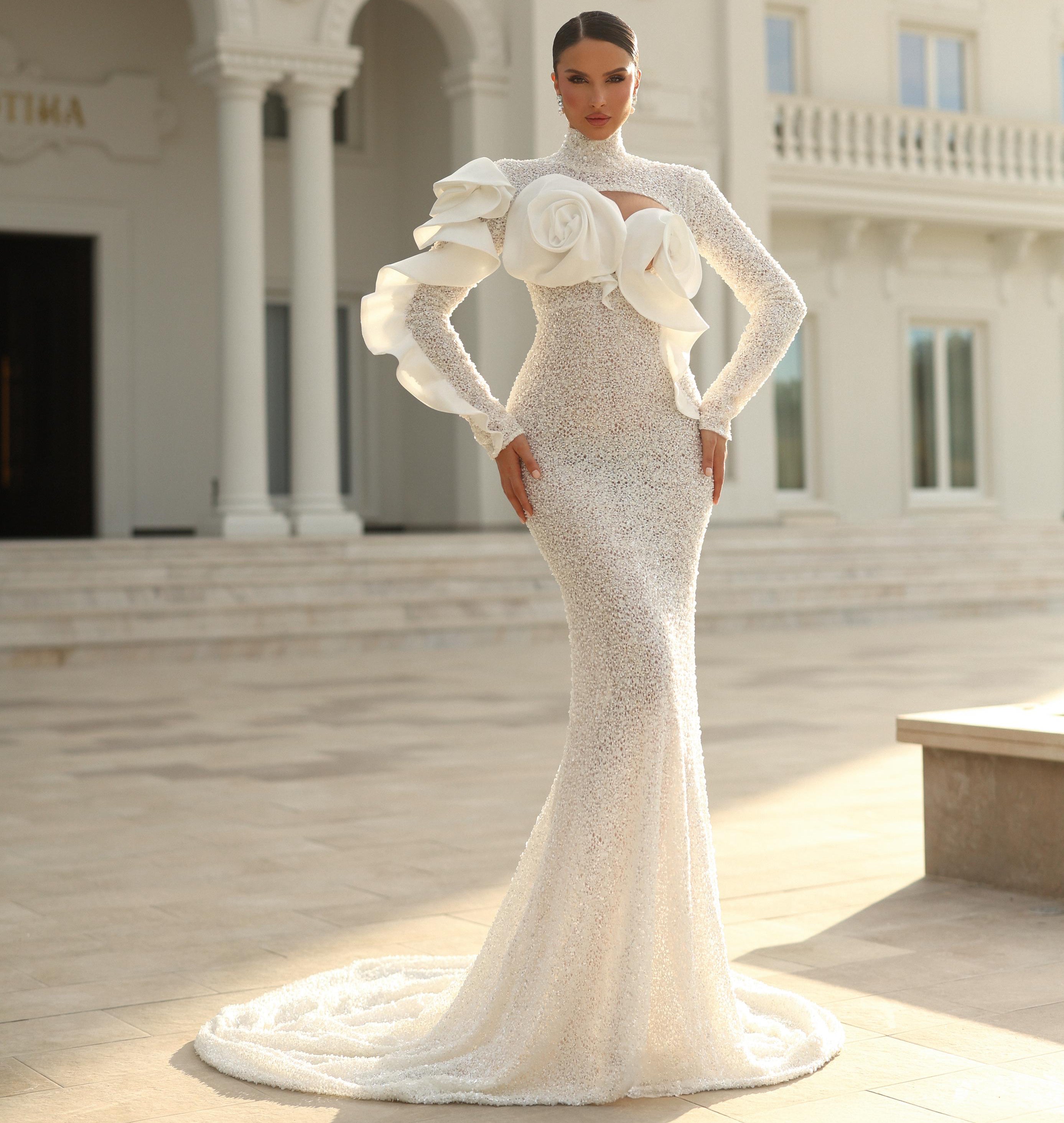 Woman in a white evening gown with floral details standing in front of an elegant building.