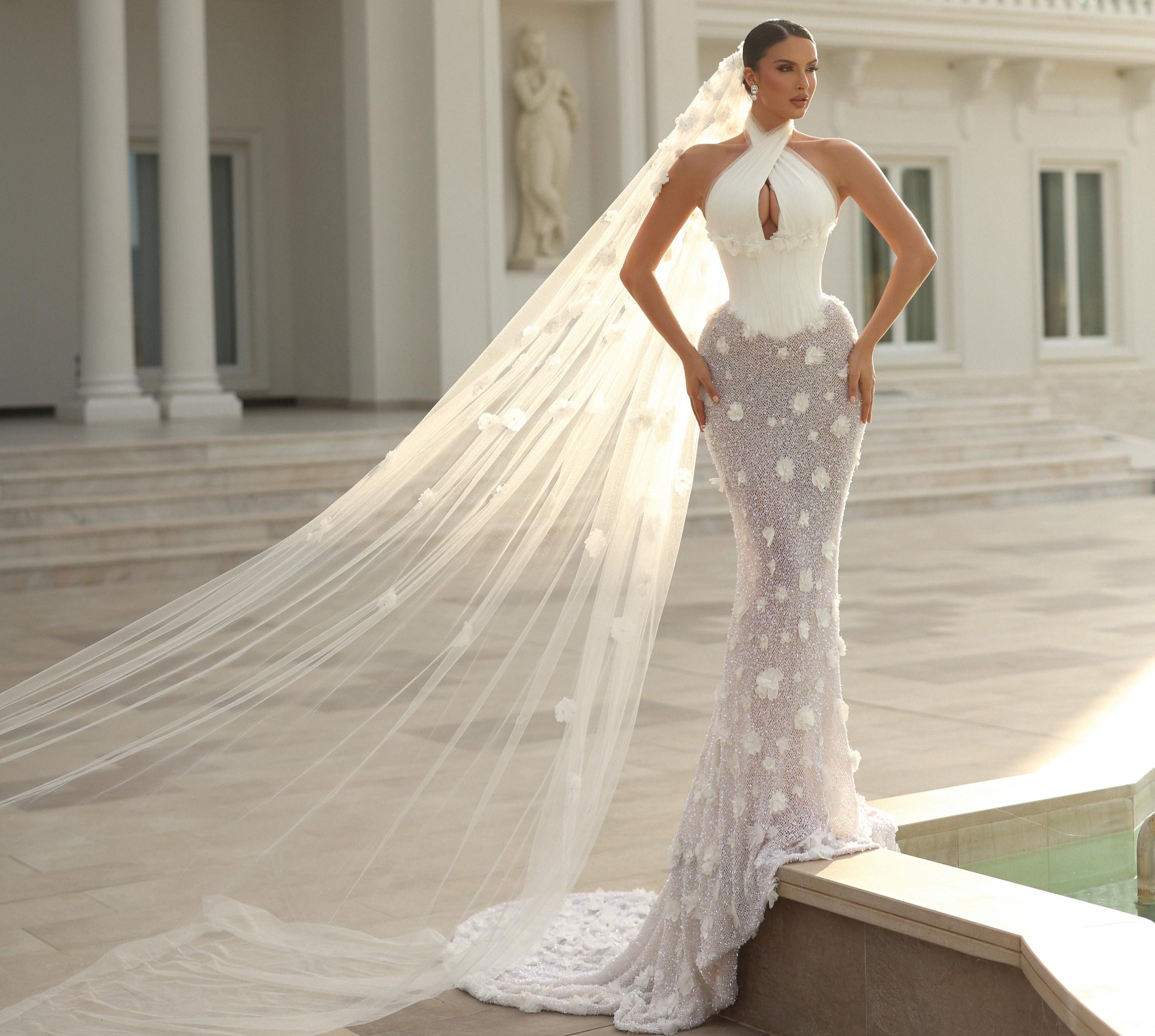 Woman in a white wedding dress with a long veil standing in front of an elegant building.