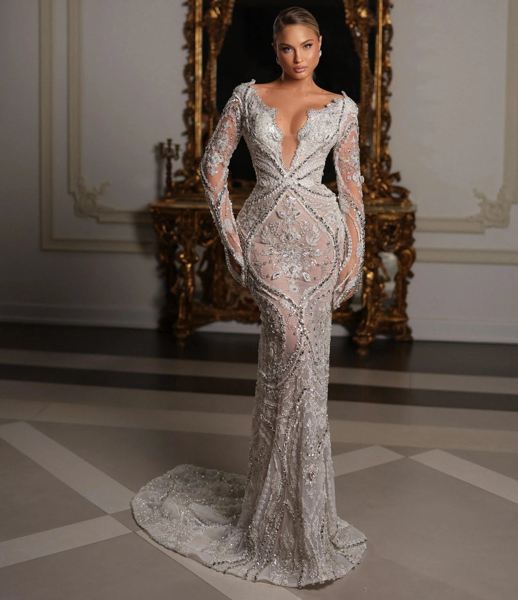 Woman in a sparkling evening gown standing in an ornate room with a large mirror.