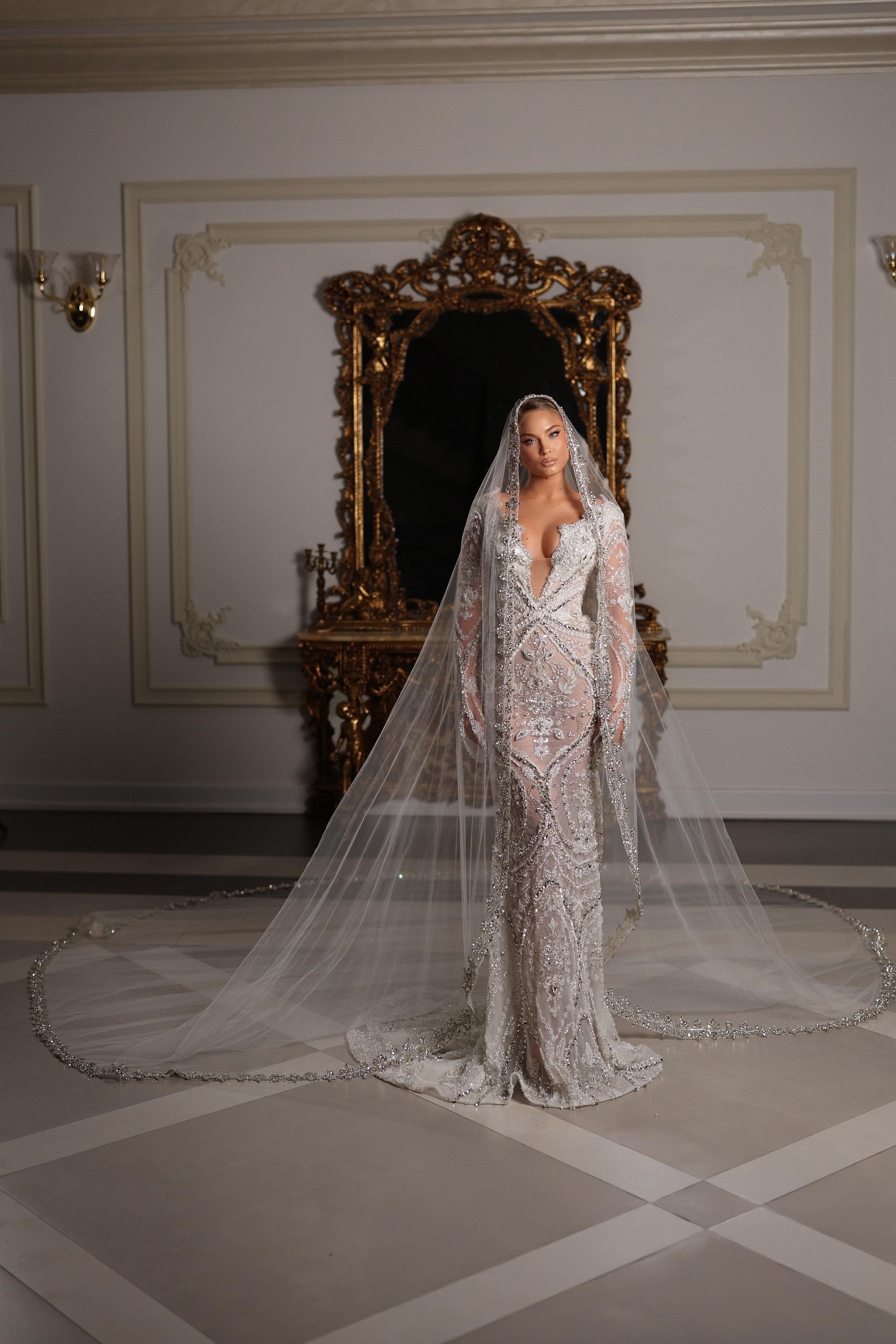 Woman in a sparkling evening gown standing in an ornate room with a large mirror.