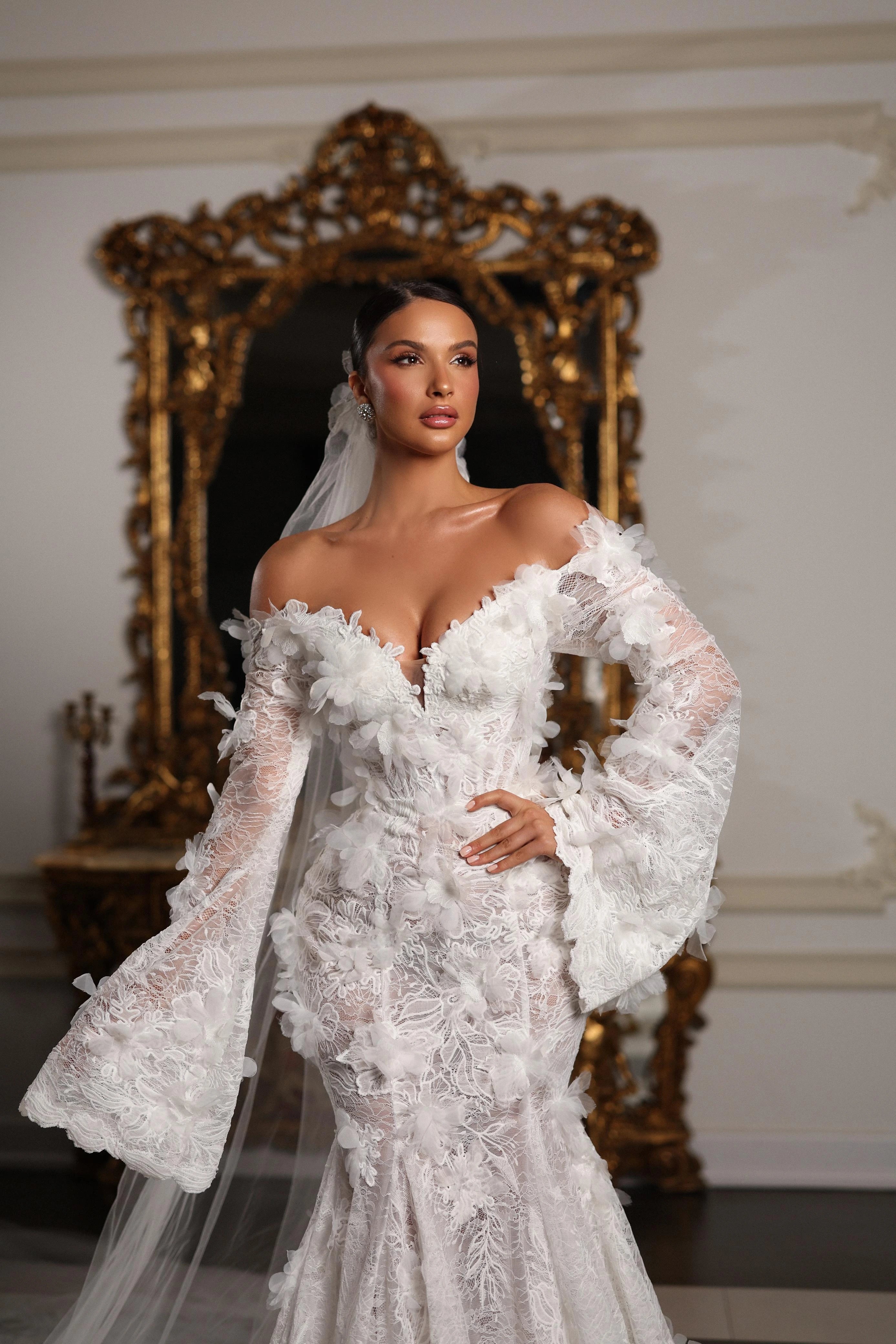 Woman in a white wedding dress standing in a room with ornate decor.