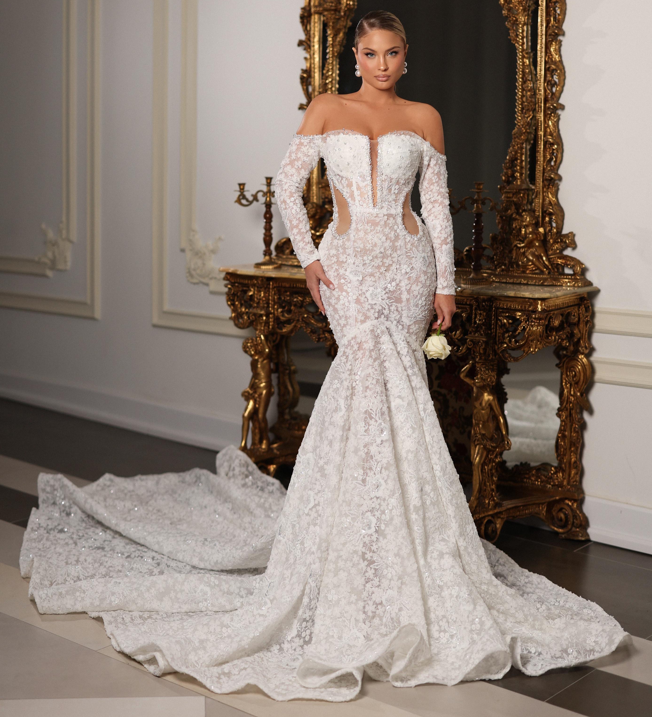Woman in a white lace wedding dress standing in front of an ornate mirror.